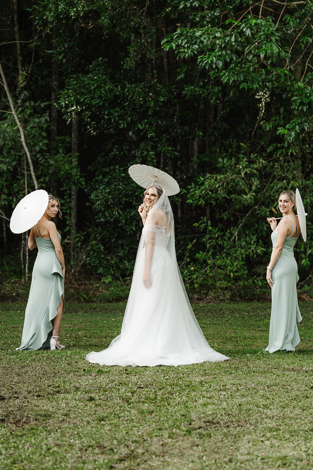 Luxury bridal editorial photo of a bride and her two bridesmaids holding elegant European-style sun umbrellas at Buderim Falls on the Sunshine Coast, captured through timeless wedding photography and videography