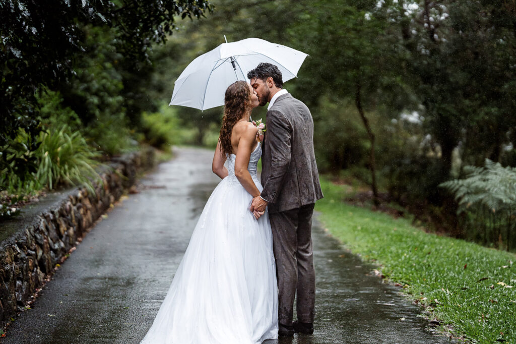 Rainy Wedding Portraits | Noosa Botanic Gardens Wedding Photographer & Videographer Bride and groom sharing a kiss during their wedding portraits at Noosa Botanic Gardens on a romantic rainy autumn afternoon.